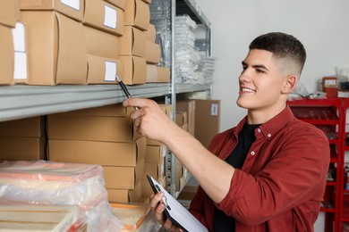 Photo of Smiling young man with clipboard near cardboard boxes in auto store
