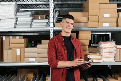Photo of Young man with clipboard near cardboard boxes in auto store