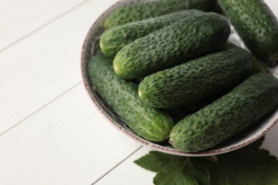 Fresh green cucumbers in bowl on white wooden table, space for text