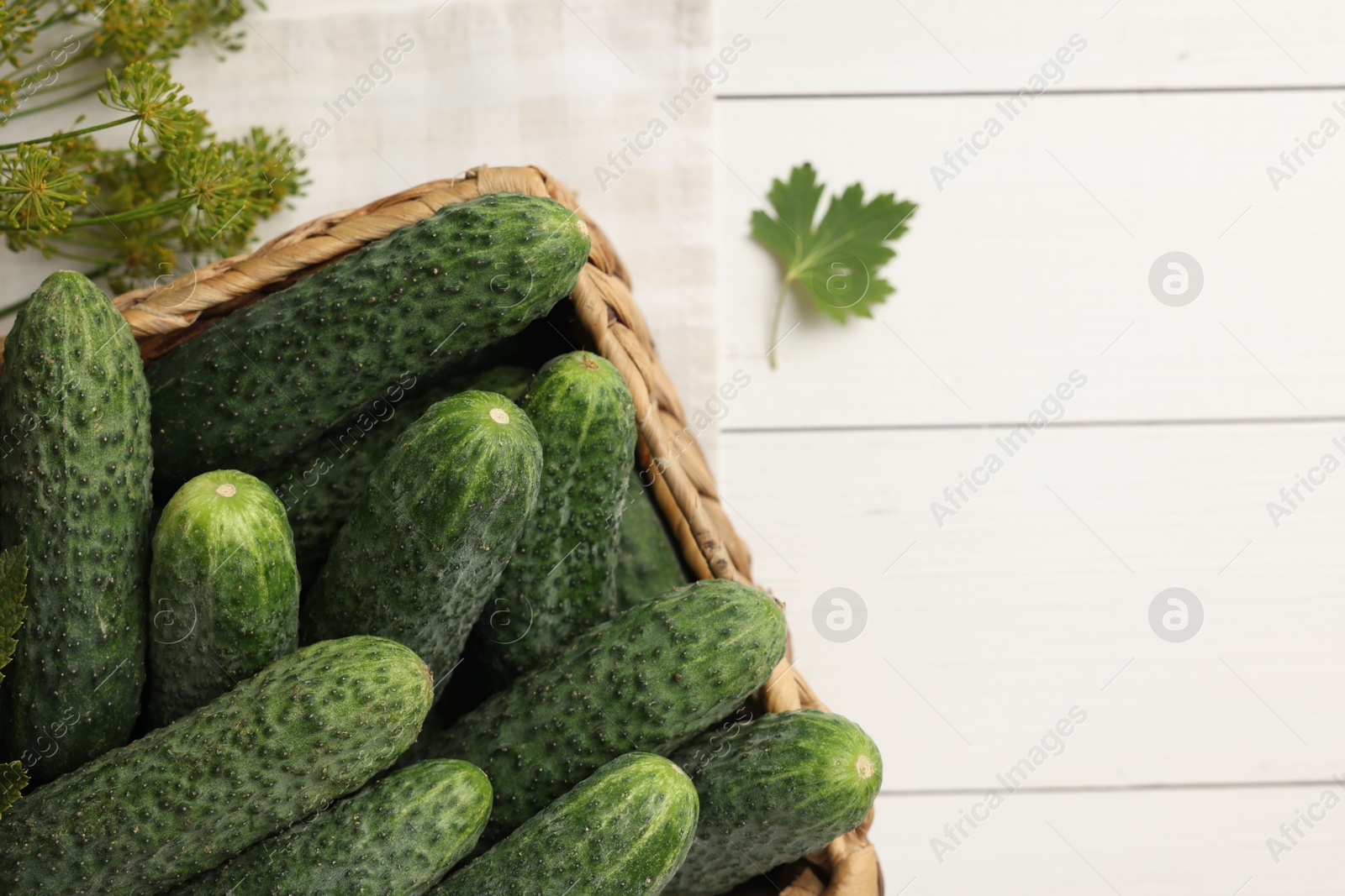 Photo of Fresh green cucumbers in box and spices on white wooden table, top view. Space for text