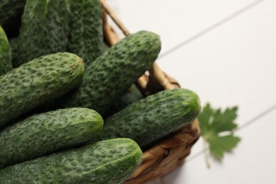 Photo of Fresh green cucumbers in wicker box on white table, closeup