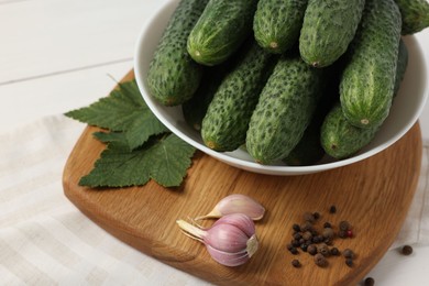 Fresh green cucumbers in bowl and spices on white table, closeup