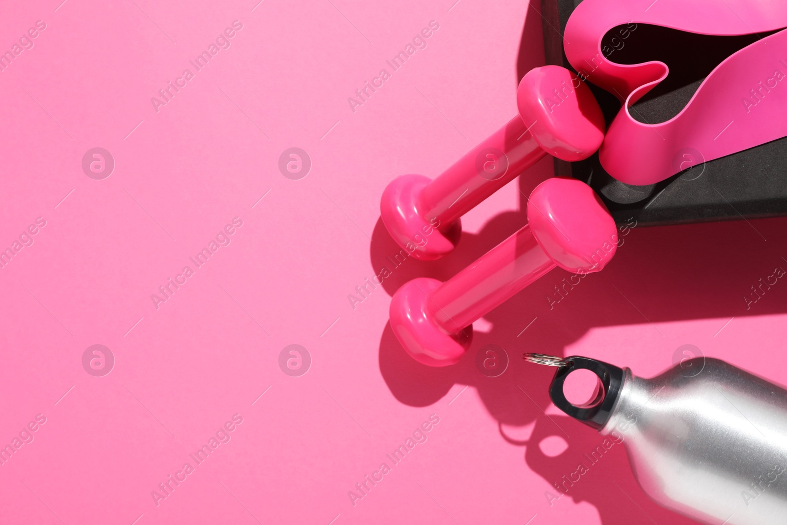 Photo of Dumbbells, fitness elastic band, water bottle and yoga block on pink background, flat lay. Space for text