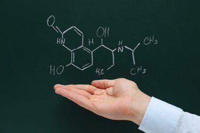 Photo of Teacher showing chemical formulas written with chalk on green chalkboard, closeup