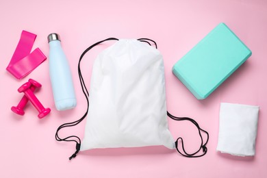 Photo of White drawstring bag and sports equipment on pink background, flat lay