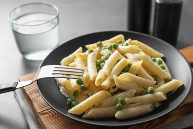Photo of Delicious pasta with green peas, cheese, fork and water on grey table, closeup