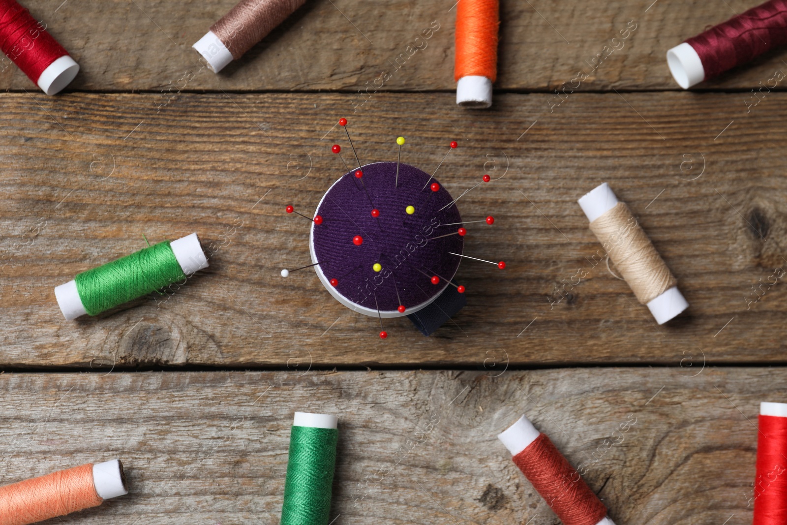 Photo of Blue pincushion with pins and spools of threads on wooden table, flat lay