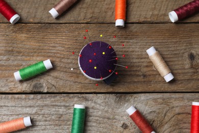 Blue pincushion with pins and spools of threads on wooden table, flat lay