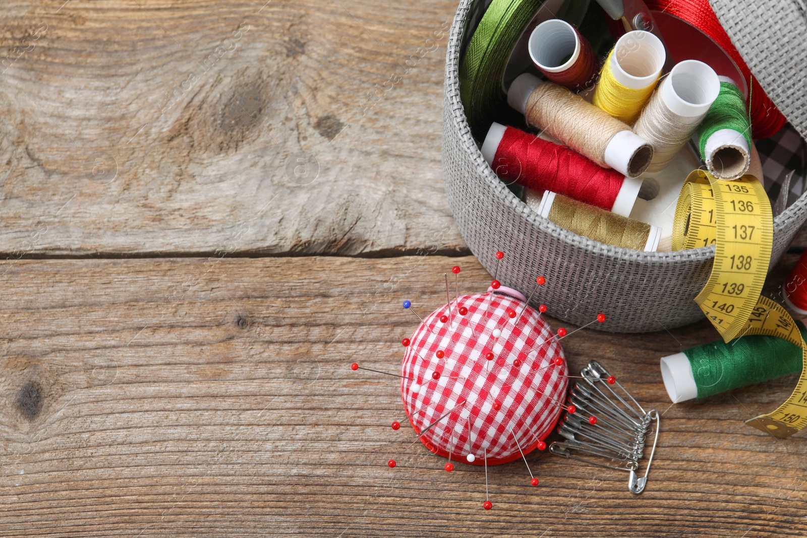 Photo of Checkered pincushion with pins and other sewing tools on wooden table, flat lay. Space for text