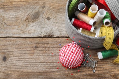 Photo of Checkered pincushion with pins and other sewing tools on wooden table, flat lay. Space for text