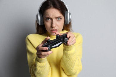 Photo of Woman in headphones playing video game with controller on light grey background, selective focus