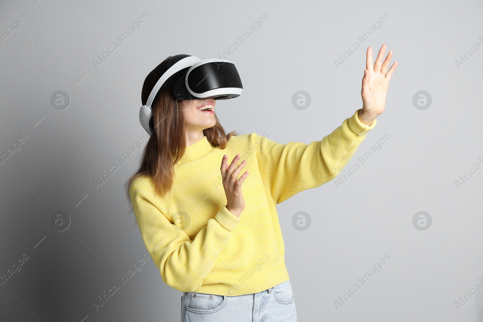 Photo of Smiling woman using virtual reality headset on light grey background