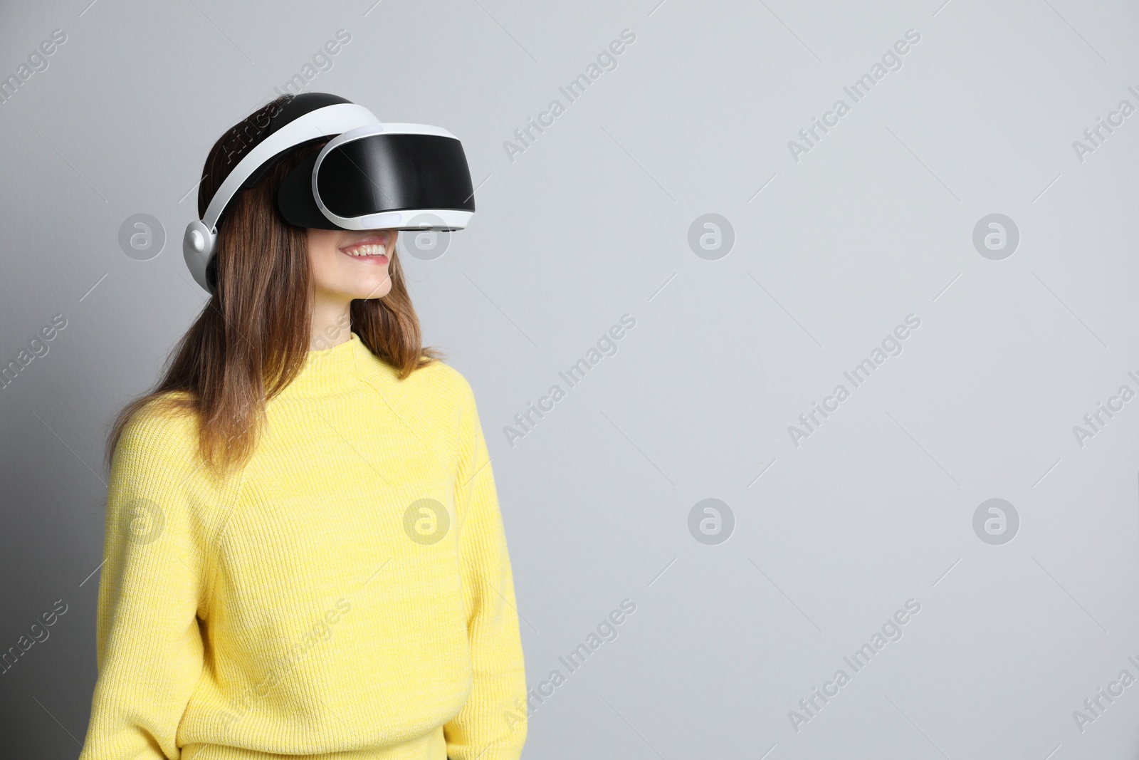 Photo of Smiling woman using virtual reality headset on light grey background. Space for text