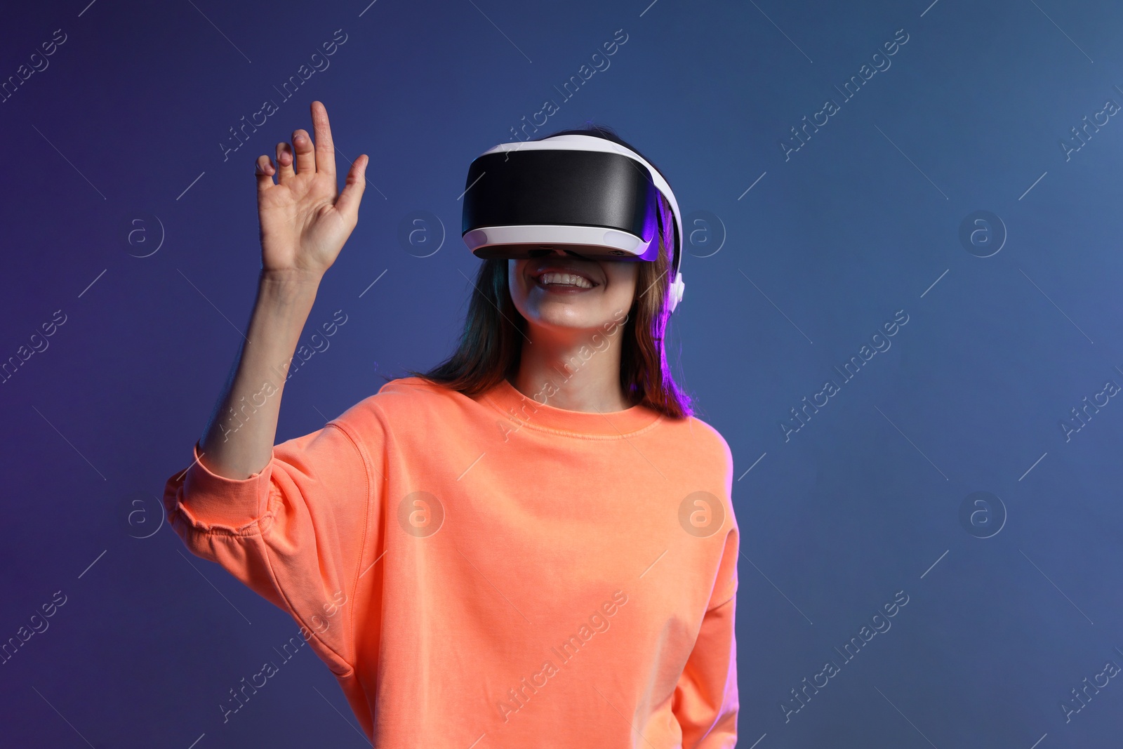 Photo of Smiling woman using virtual reality headset on dark blue background