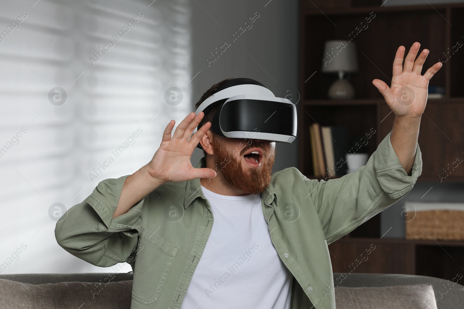 Photo of Emotional man using virtual reality headset on sofa at home