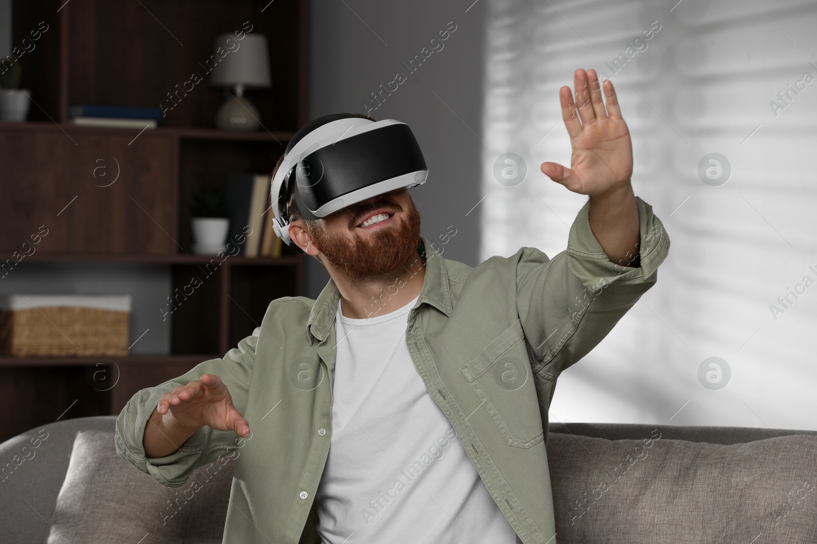 Photo of Smiling man using virtual reality headset on sofa at home