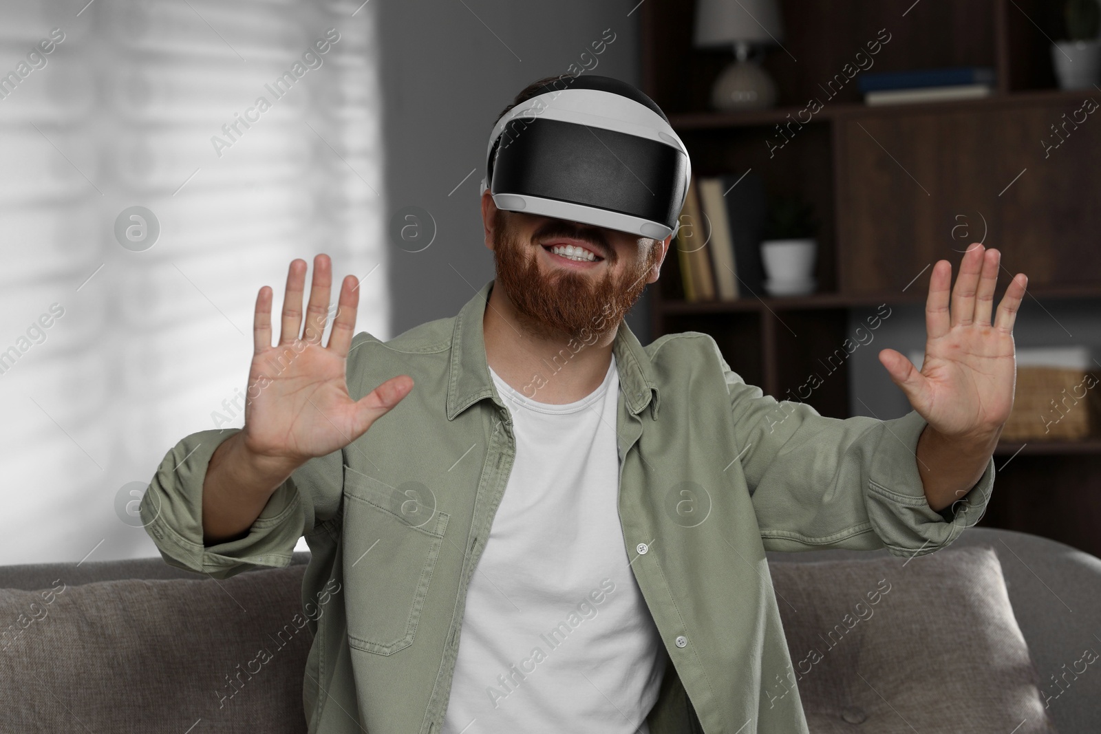 Photo of Smiling man using virtual reality headset on sofa at home