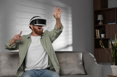 Photo of Emotional man using virtual reality headset on sofa at home. Space for text