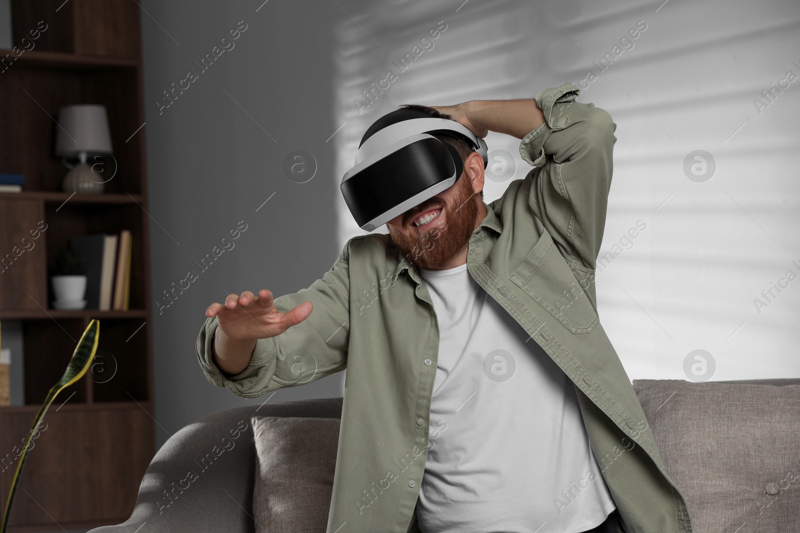 Photo of Smiling man using virtual reality headset on sofa at home