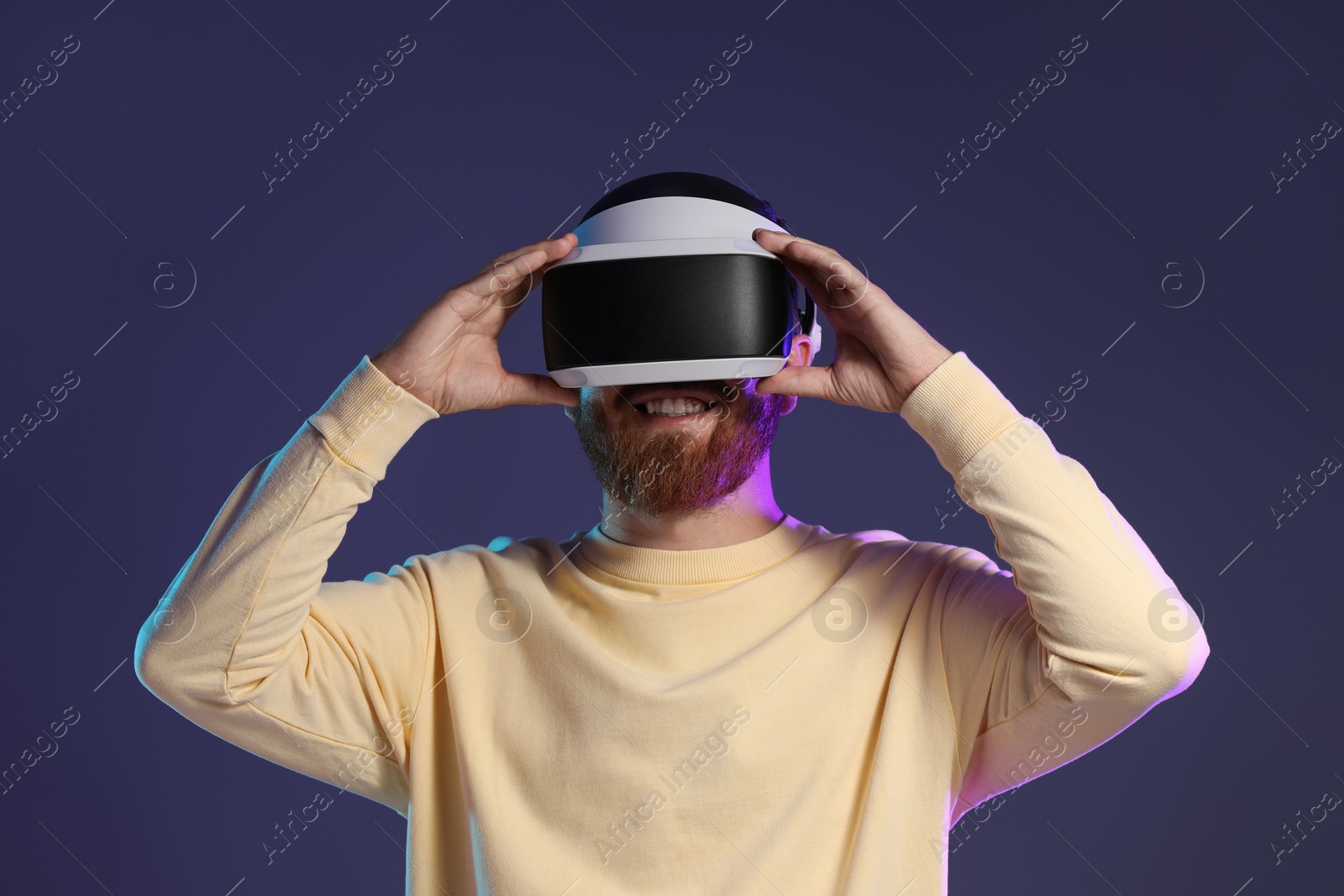 Photo of Smiling man using virtual reality headset on dark purple background