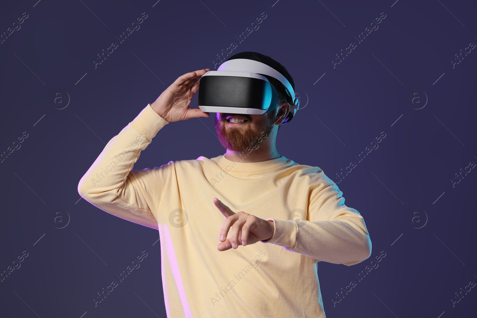 Photo of Smiling man using virtual reality headset on dark purple background