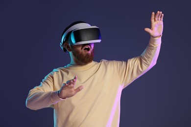 Photo of Emotional man using virtual reality headset on dark purple background