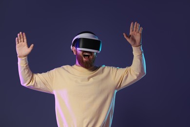 Photo of Emotional man using virtual reality headset on dark purple background