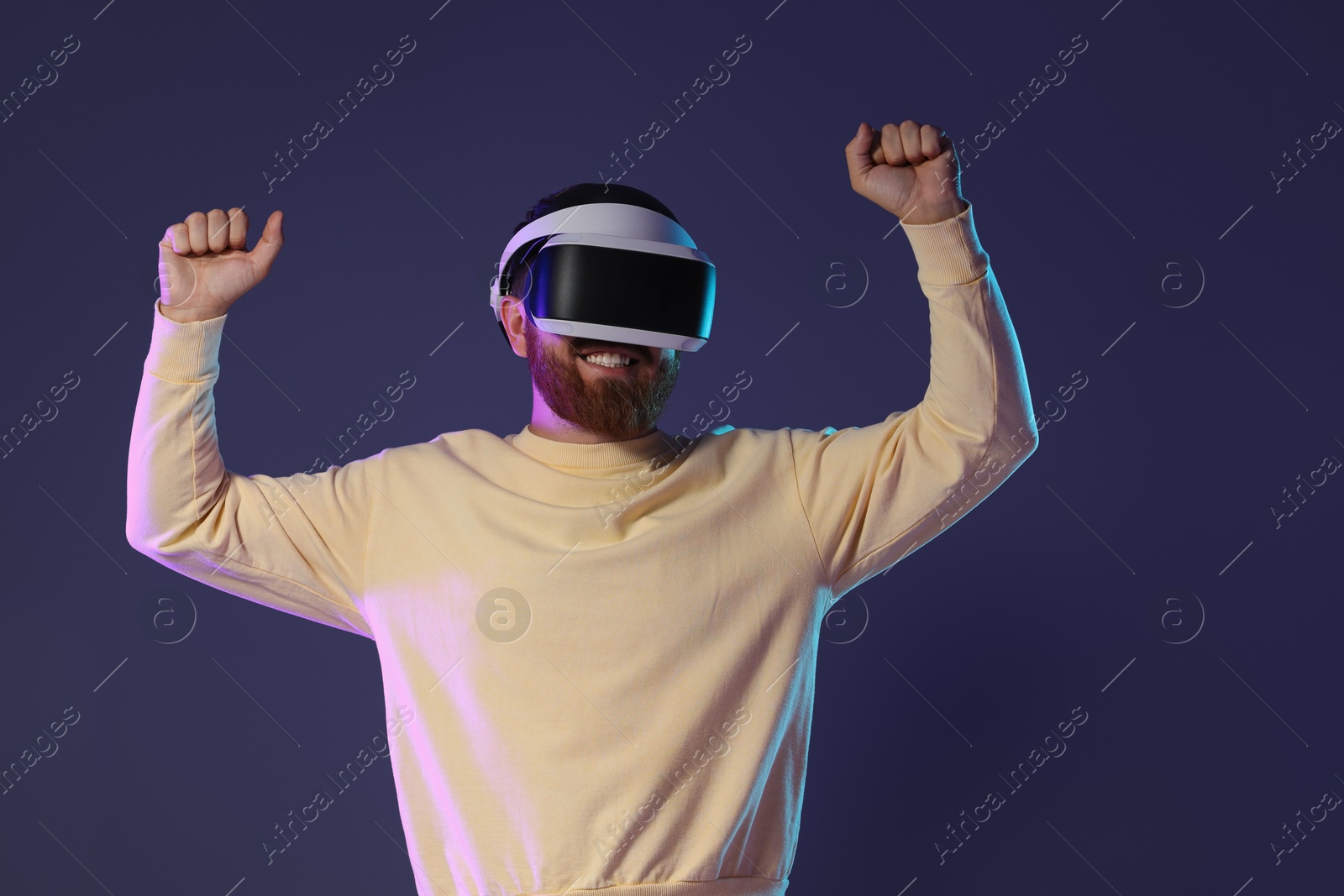 Photo of Smiling man using virtual reality headset on dark purple background