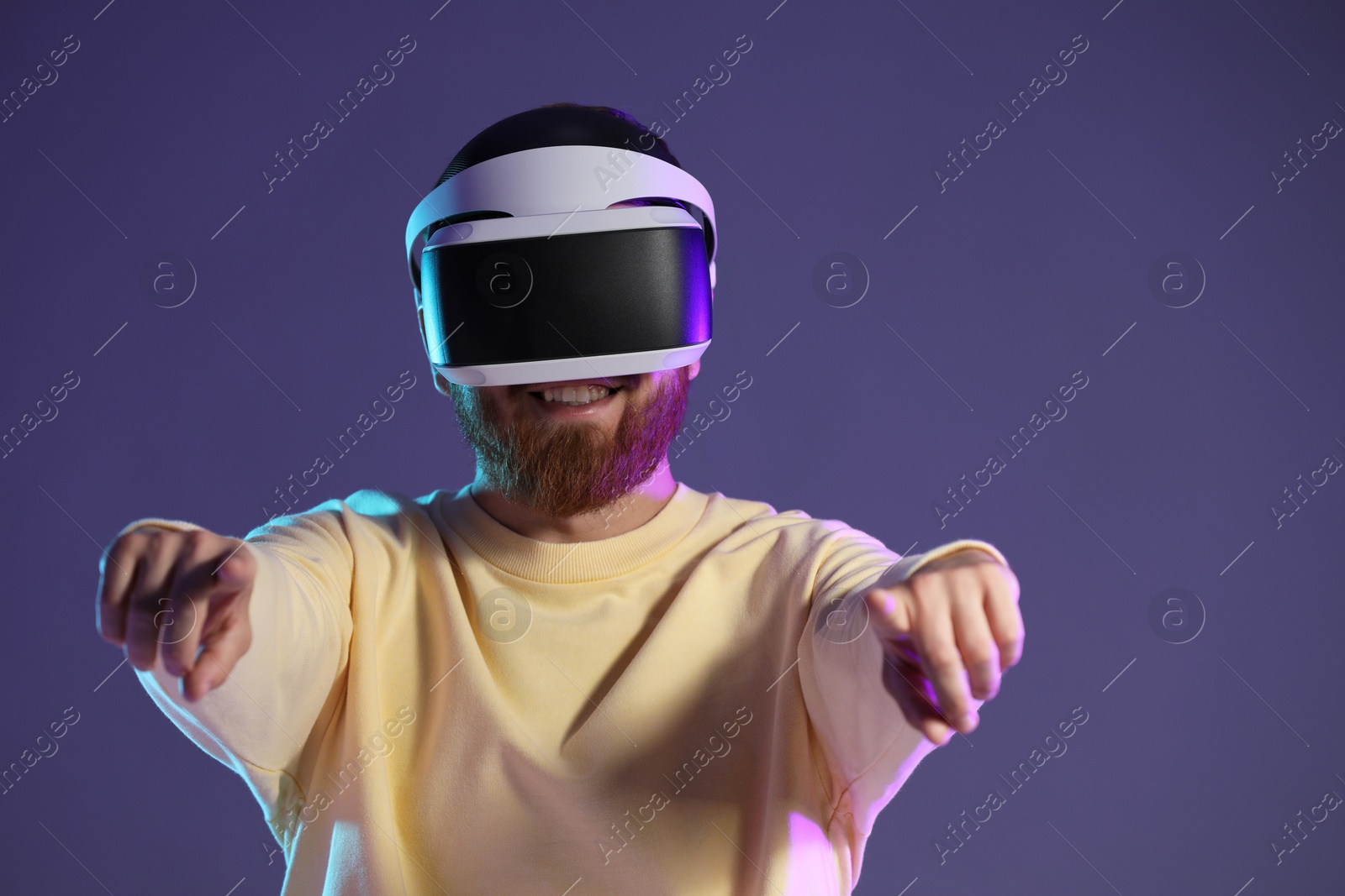 Photo of Smiling man using virtual reality headset on dark purple background