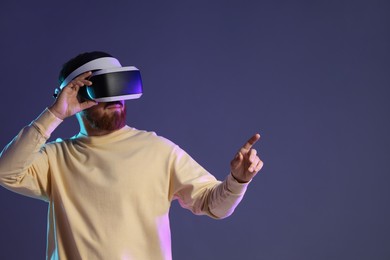 Photo of Man using virtual reality headset on dark purple background. Space for text