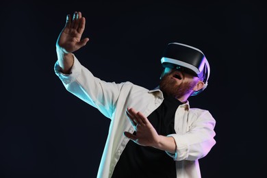 Photo of Emotional man using virtual reality headset on dark background in neon lights