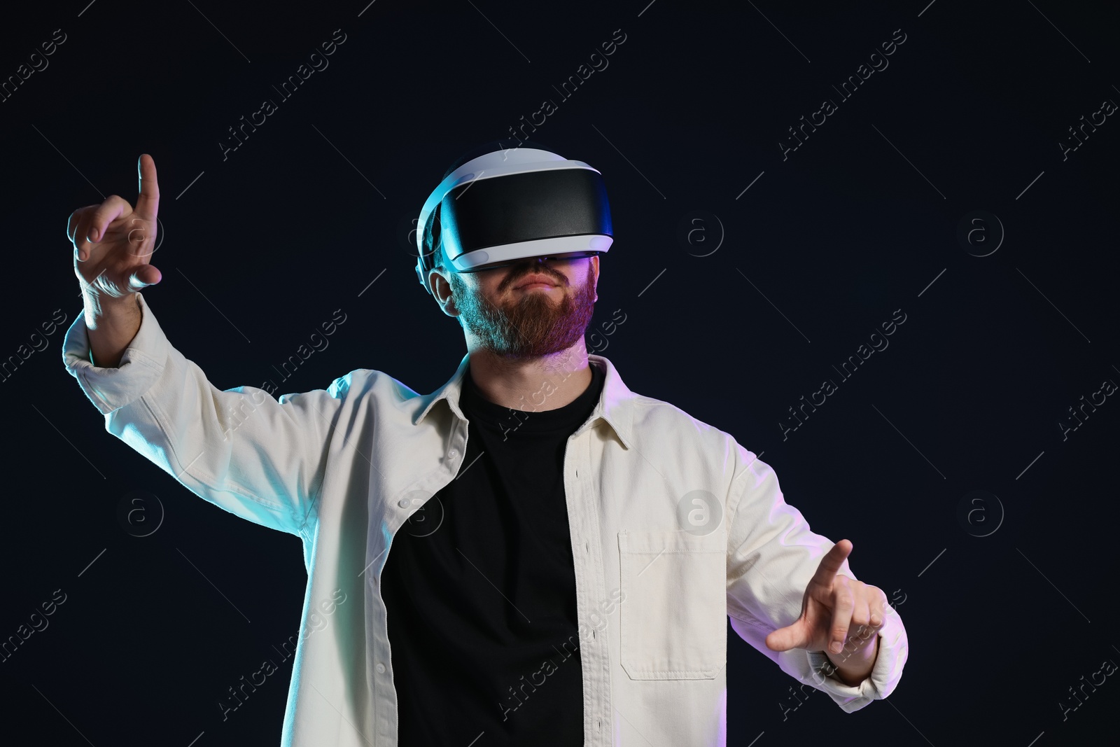 Photo of Man using virtual reality headset on dark background in neon lights