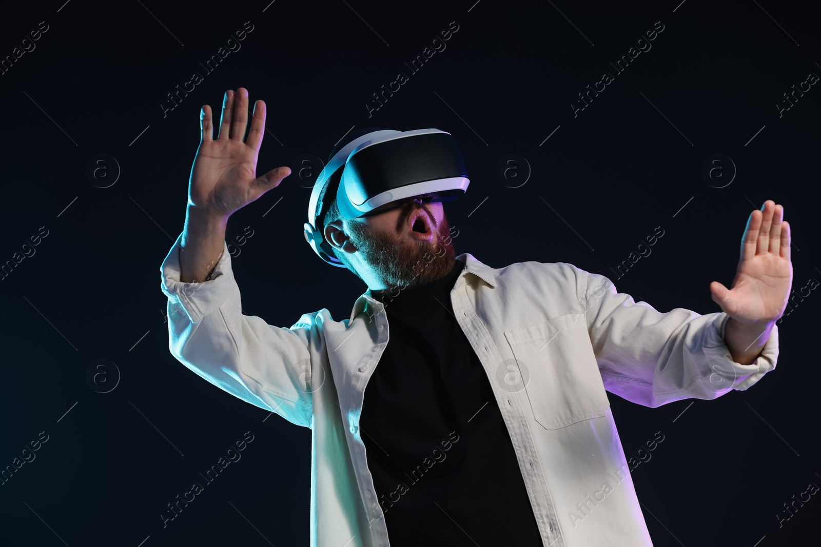 Photo of Emotional man using virtual reality headset on dark background in neon lights