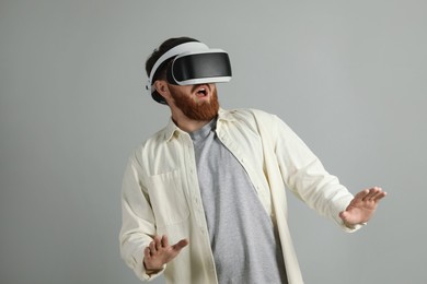 Photo of Emotional man using virtual reality headset on grey background