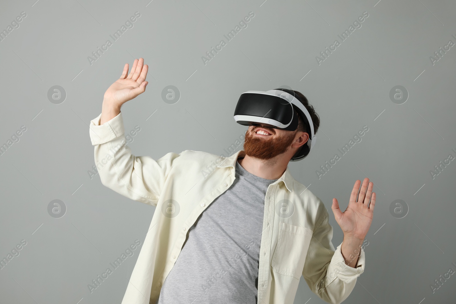 Photo of Smiling man using virtual reality headset on grey background