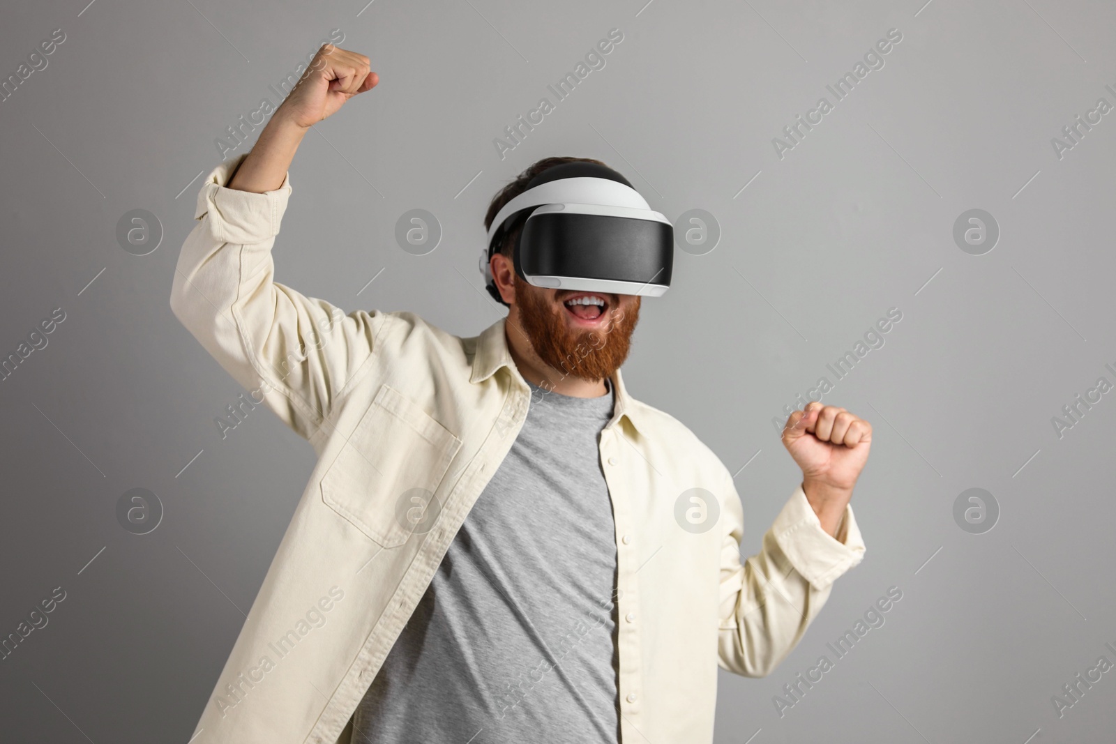 Photo of Smiling man using virtual reality headset on grey background