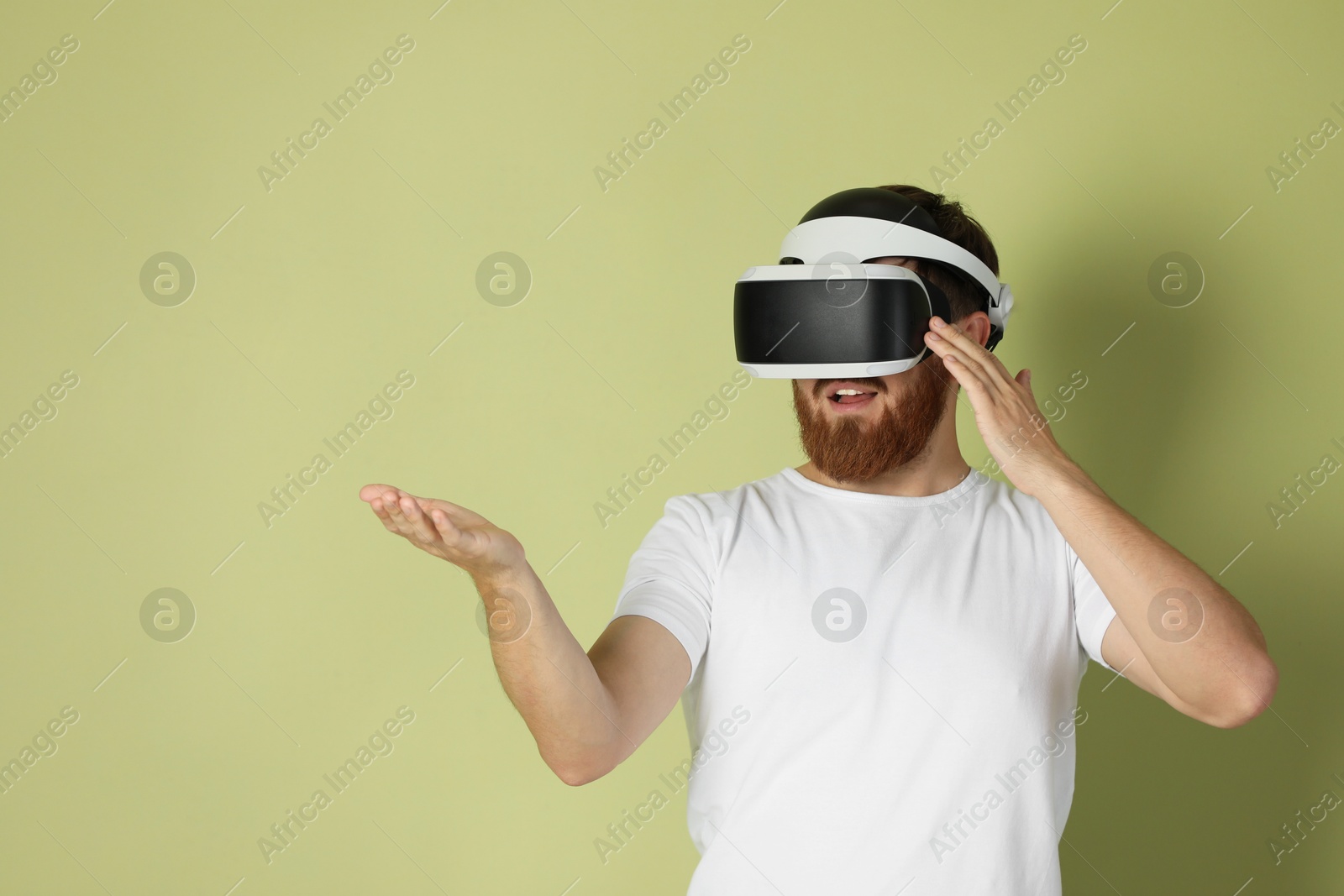 Photo of Smiling man using virtual reality headset on pale green background. Space for text