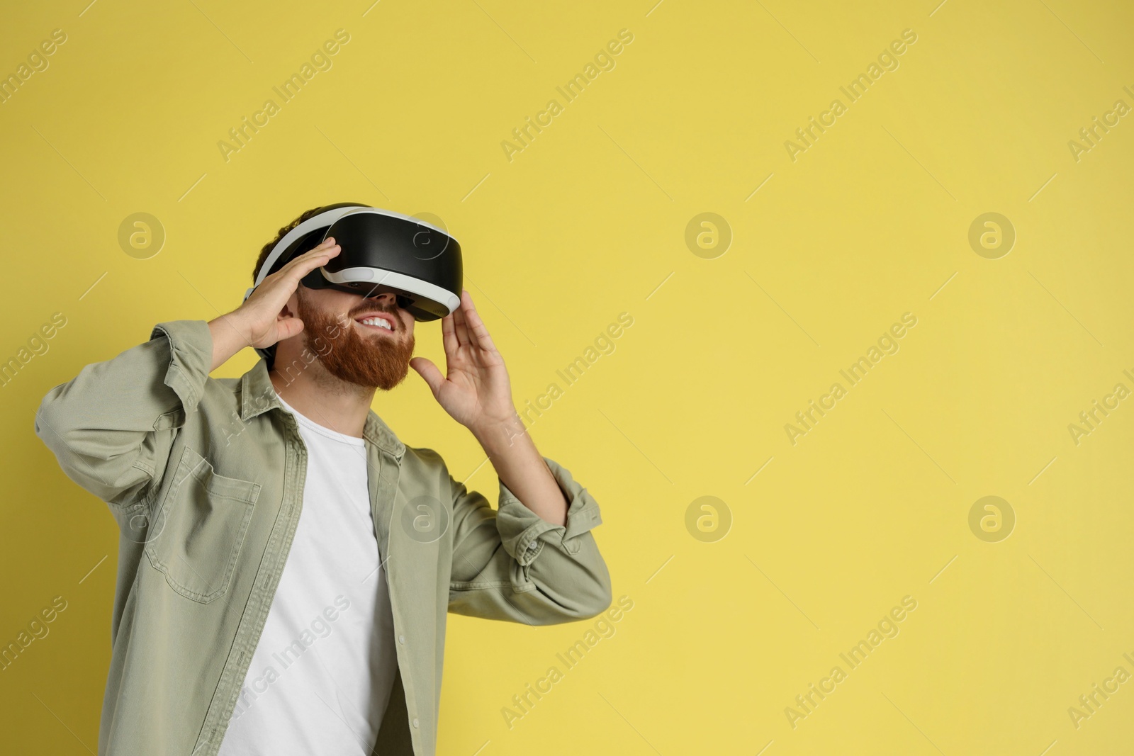 Photo of Happy man using virtual reality headset on pale yellow background. Space for text