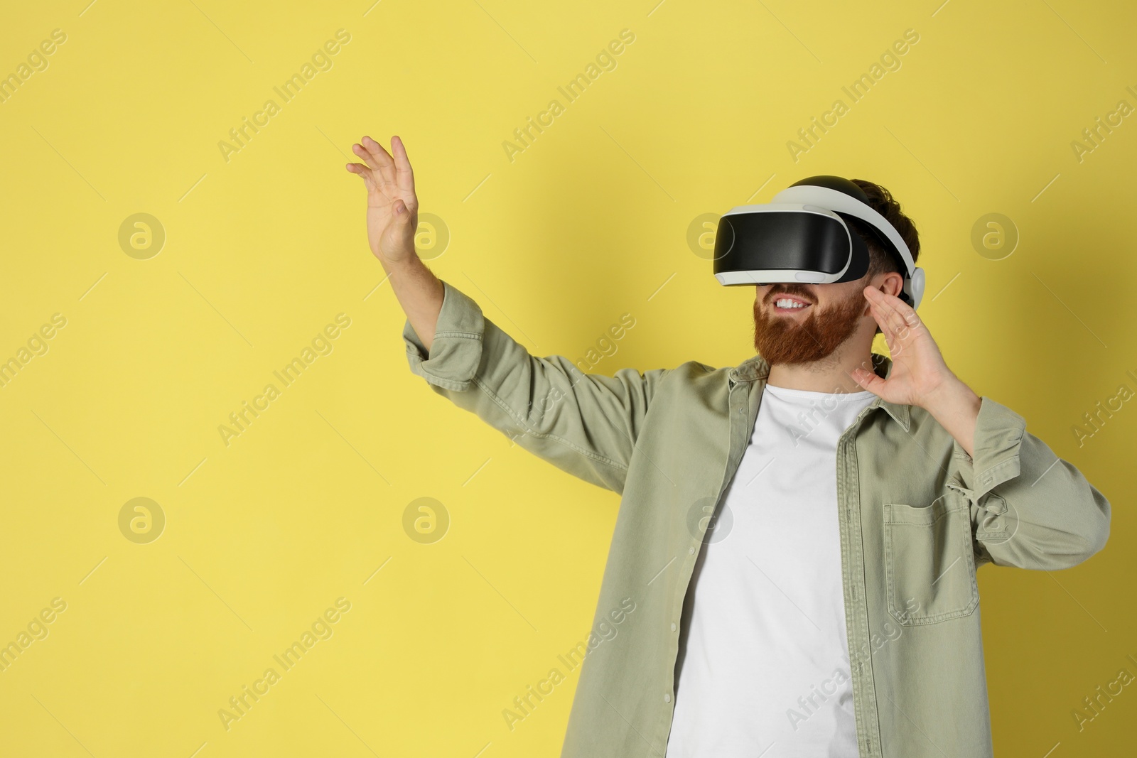 Photo of Happy man using virtual reality headset on pale yellow background. Space for text