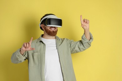 Photo of Happy man using virtual reality headset on pale yellow background
