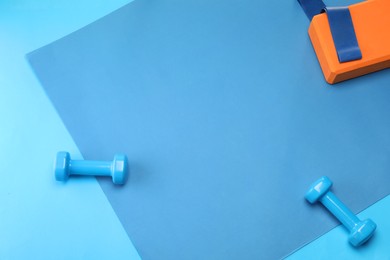 Photo of Two dumbbells, yoga block and fitness elastic band on blue background, flat lay. Space for text