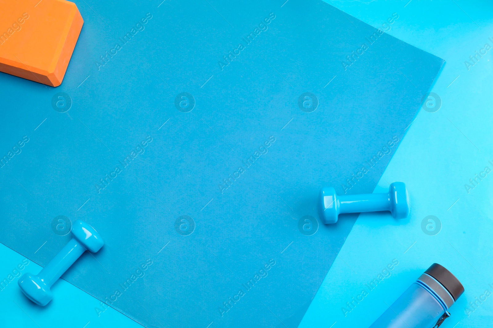 Photo of Two dumbbells, yoga block and bottle on blue background, flat lay. Space for text