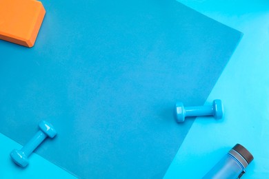 Photo of Two dumbbells, yoga block and bottle on blue background, flat lay. Space for text