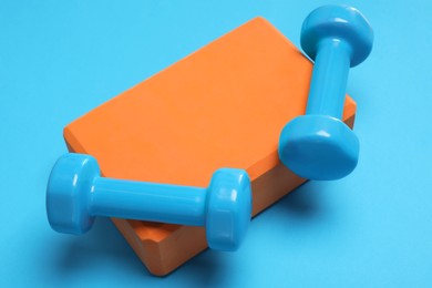Photo of Two dumbbells and yoga block on light blue background, closeup