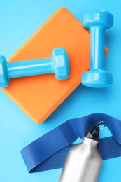 Photo of Two dumbbells, yoga block, fitness elastic band and thermo bottle on light blue background, flat lay