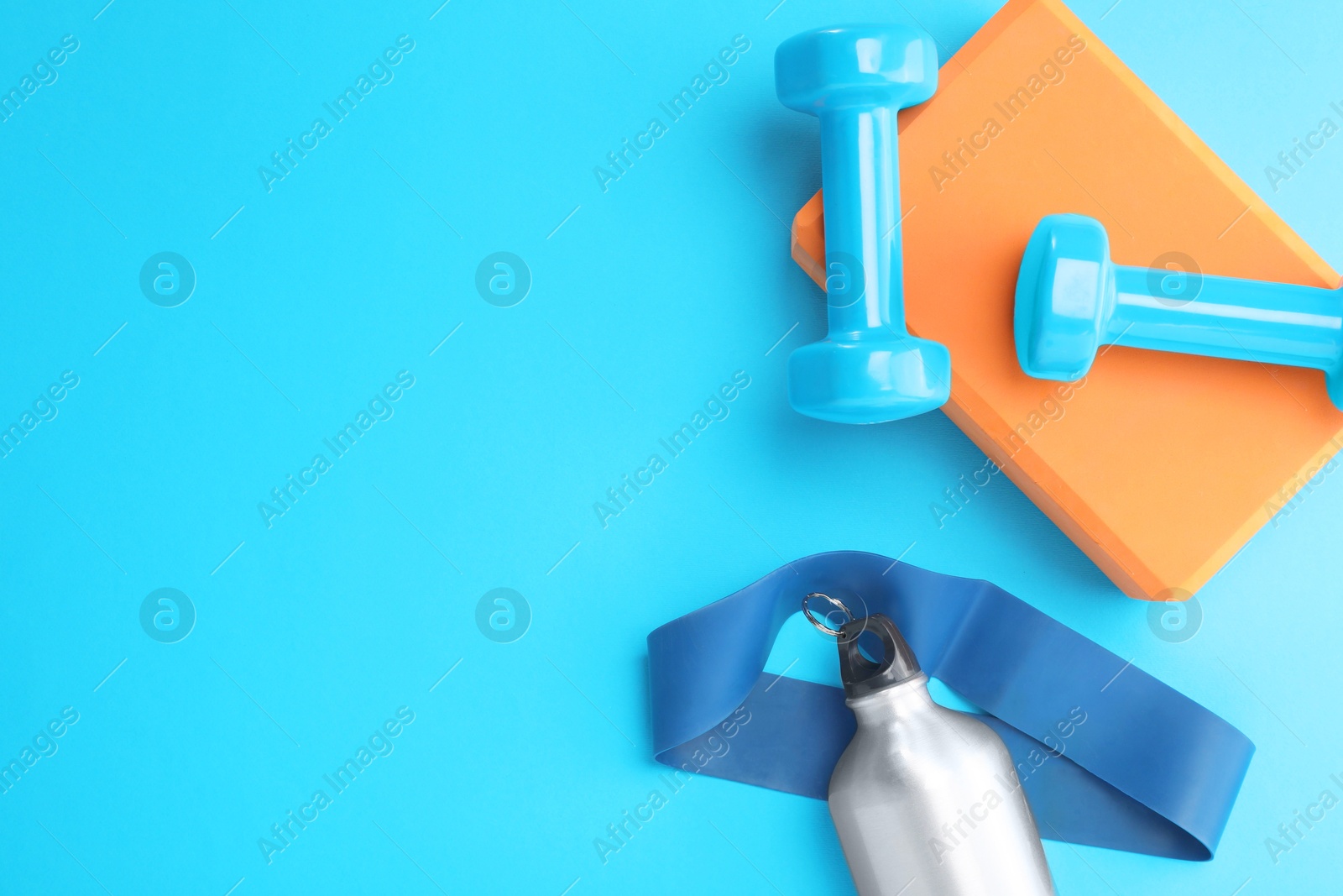 Photo of Two dumbbells, yoga block, fitness elastic band and thermo bottle on light blue background, flat lay. Space for text