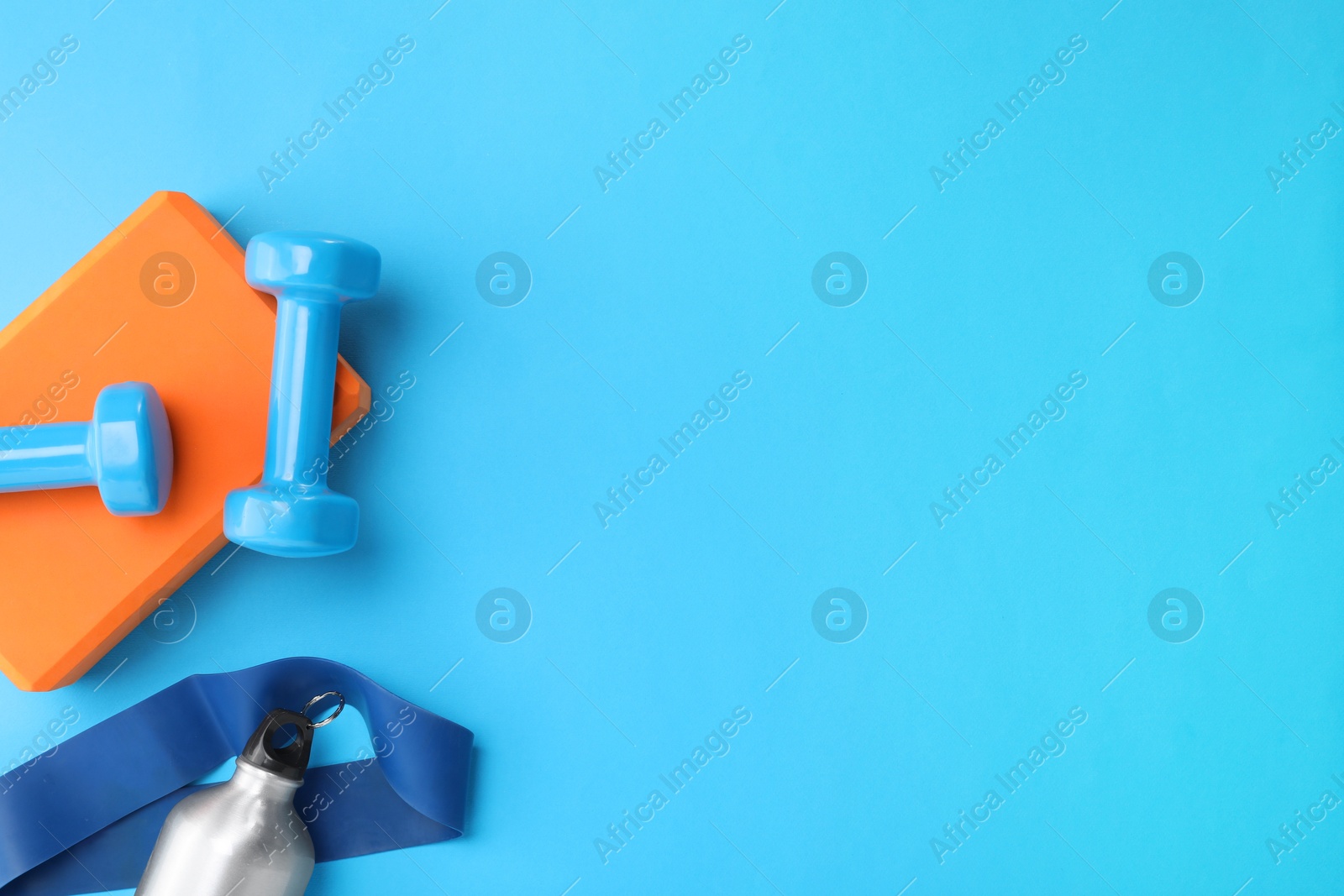 Photo of Two dumbbells, yoga block, fitness elastic band and thermo bottle on light blue background, flat lay. Space for text