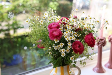 Beautiful ranunculus flowers and chamomiles in vase on windowsill indoors