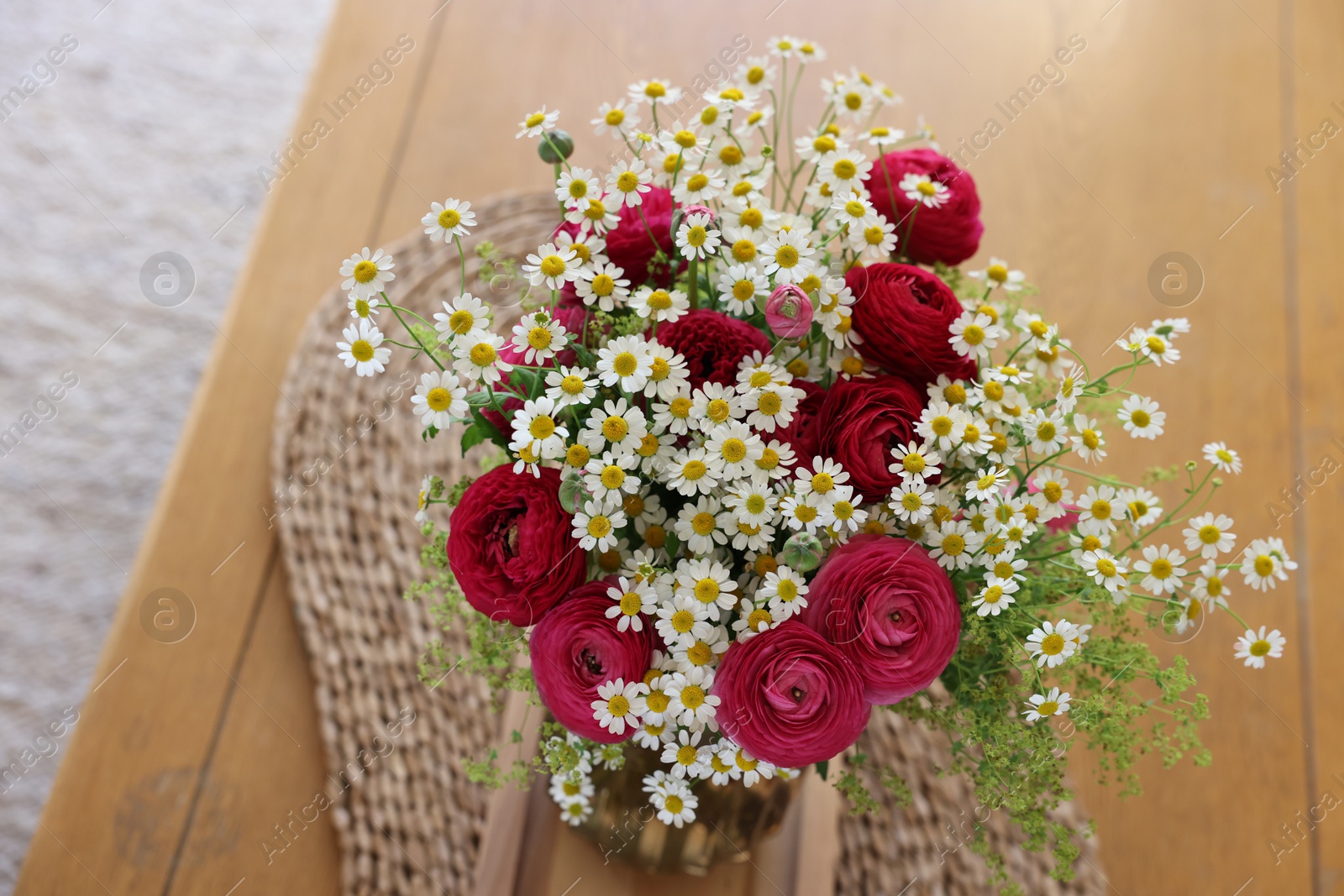 Photo of Beautiful ranunculus flowers and chamomiles in vase on table indoors, above view