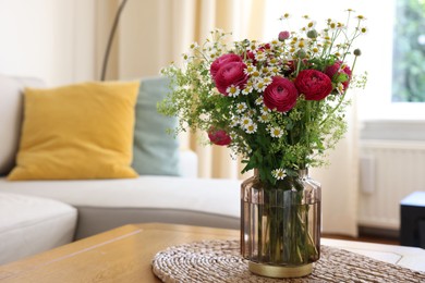 Beautiful ranunculus flowers and chamomiles in vase on table indoors